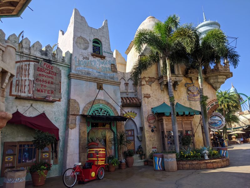 A graffitied building with a red and yellow bike in front and two palm trees
